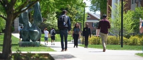 Multiple students walking to class on a sunny day near the flame statue